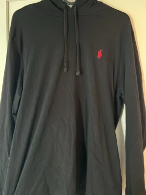 Svart hoodie från Polo Ralph Lauren - Svart tunn hoodie från Polo Ralph Lauren med klassisk huva och dragsko. Liten röd logga på bröstet. Hoodien är i storlek S och i mycket bra skick. Tillverkad i mjuk bomull som känns skön mot huden. Hör av er vid funderingar!