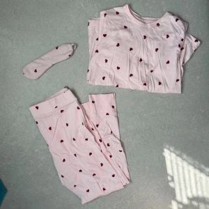 Rosa pyjamas med röda hjärtan - Söt rosa pyjamas från Cubus i storlek M med långärmad tröja, byxor och matchande sovmask. Alla delar har ett gulligt mönster av små röda hjärtan!❤️