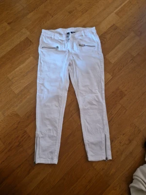 Vita trekvarts skinny jeans med dragkedjor - Säljer ett par vita skinny jeans från KappAhl med coola dragkedjor vid fickorna och bensluten. Jeansen har normal midja, bälteshällor och är tillverkade i ett stretchigt bomullsmaterial för skön passform. Perfekta för en fräsch och trendig look!