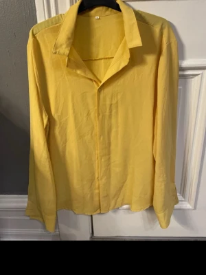 Gul långärmad skjorta i bomull - Snygg gul skjorta med klassisk krage och långa ärmar. Skjortan är tillverkad i mjuk bomull och har en enkel, clean design utan mönster eller detaljer. Perfekt för dig som vill ha en färgklick i garderoben.