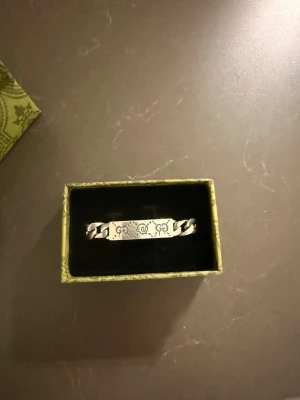 Cuban Chain Skull Gucci Armband S925 - Skaffa dig en  armband från Gucci med gravyrdetaljer och kraftig kedja med den ikoniska GG märket. Armbandet har en rektangulär platta med Gucci-logga och dekorativa mönster. Perfekt accessoar för dig som gillar exklusiv och stilren design.                                                                                         Priset kan förhandlas vid snabbaffär.                 Nypris: ca 3500kr