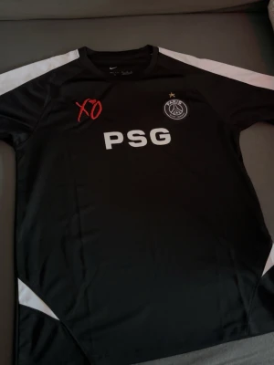 Psg tröja - Säljer en svart PSG XO tröja från Nike med vita detaljer på axlar och sidor. PSG-logga och XO-brodyr på bröstet samt stor vit PSG-text framtill. Tillverkad i ett lätt och sportigt material, perfekt för träning eller streetwear.