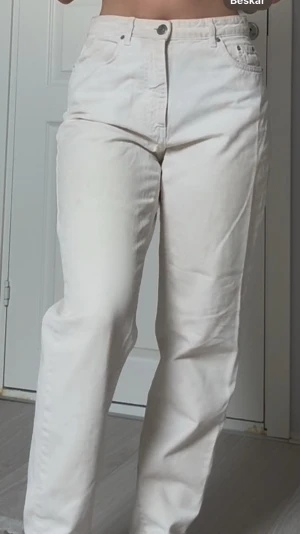 Vit-beiga raka jeans med hög midja - Säljer ett par vita jeans med rak passform och hög midja. Klassisk femficksmodell med knapp och dragkedja framtill. Jeansen har en clean look utan slitningar eller detaljer och är tillverkade i ett tjockare bomullstyg.