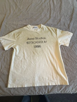 Vit Acne Studios t-shirt Stockholm - Vit t-shirt från Acne Studios med trycket 'STOCKHOLM 1996' på bröstet. Klassisk rund hals och korta ärmar. Tillverkad i mjuk bomull för en bekväm känsla och enkel stil.