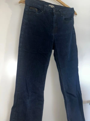 Mörkblå jeans  - Snygga mörkblå jeans med glansigt typ. Rak passform och vida nere vid benen. Klassisk femficksmodell med bälteshällor. Perfekta för dig som gillar en stilren men ändå unik look.
