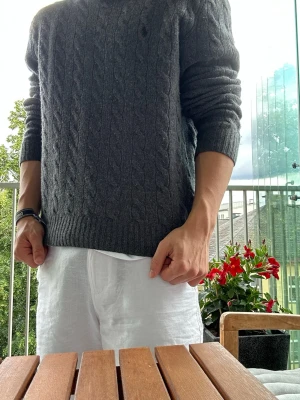 Grå kabelstickad kashmir tröja Polo Ralph Lauren - Mörkgrå kabelstickad tröja från Polo Ralph Lauren. Klassisk modell med rund halsringning och ribbade muddar vid ärmslut och nederkant. Perfekt för lager-på-lager och snygg till både jeans och chinos. Den har blivit lite krympt i tvätten men ska fortfarande kunna passa på M eller S