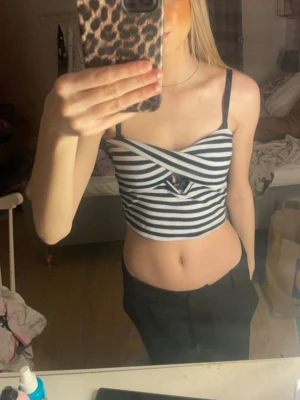 Randig croppad linnetopp - Säljer en croppad linnetopp med svarta och vita ränder. Toppen har smala axelband, omlottdetalj framtill och en liten cut-out vid bysten. Perfekt för dig som gillar trendiga och somriga plagg.