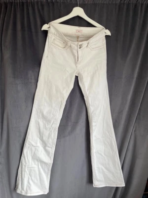 Vita bootcut jeans från Nelly  - Säljer ett par vita bootcut jeans från nelly med snygga kontrastsömmar och klassiska fem fickor. Jeansen har en låg midja och utsvängda ben, samt dekorativa sömmar på bakfickorna. Perfekta för en trendig och avslappnad stil.