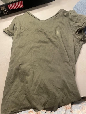 Olivgrön t-shirt från Ralph Lauren - Säljer en olivgrön t-shirt från Ralph Lauren med klassisk rund hals och korta ärmar. T-shirten har en liten broderad logga på bröstet och är gjord i mjuk bomull. Perfekt för chill dagar och enkel att matcha med jeans eller shorts.