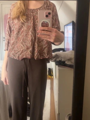 Brun paisleymönstrad blus - Säljer en luftig brun blus med paisleymönster i beige och rödtoner. Blusen har rund halsringning och långa ärmar med avslappnad passform. Perfekt för dig som gillar boho-stil och mjuka material.🩷🩷