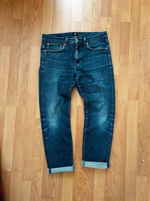 Mörkblå selvedge Edwin jeans - Säljer ett par mörkblå selvedge edwin jeans med snygga slitningar och upprullade benslut. Klassisk femficksmodell med vita sömmar och diskret logga på bakfickan. Jeansen är i ett mjukt denimtyg och har en rak passform som passar till det mesta.