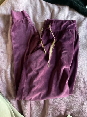 Lila velourmjukisbyxor med snöre - Säljer ett par lila mjukisbyxor i mjuk velour med bred resår i midjan och glittriga snören med metalländar. Perfekta för chill dagar hemma eller när du vill vara extra comfy. Snyggt avslappnad passform och stretchigt material.