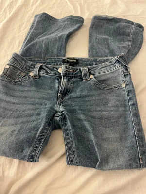 Blå bootcut jeans från True Religion - (Sydda efter min längd 160)Säljer ett par klassiska blå bootcut jeans från True Religion. Jeansen har fem fickor, snygga kontrastsömmar och silverfärgade nitar. Tillverkade i denim med en lätt tvättad look och låg midja. Perfekta för en avslappnad och trendig stil.