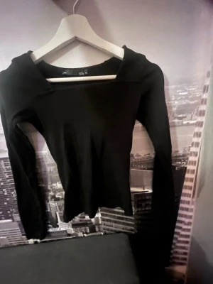 Svart långärmad topp med bred urringning - Säljer en svart långärmad topp med bred urringning. Toppen har en slim passform och är tillverkad i mjukt stretchigt material som sitter snyggt på kroppen. Perfekt att styla med jeans eller kjol för en clean look.
