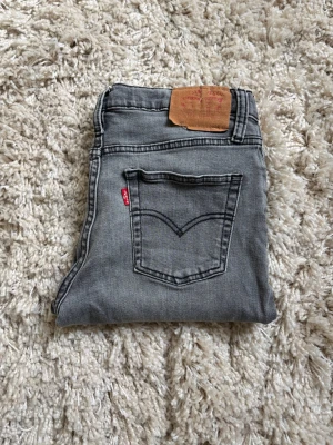 Grå Levi's 501 jeans - Säljer ett par klassiska grå Levi's 501 jeans med raka ben och femficksmodell. Jeansen har den ikoniska röda Levi's-lappen på bakfickan och patch i läder bak i midjan. Perfekta för en avslappnad och trendig look.