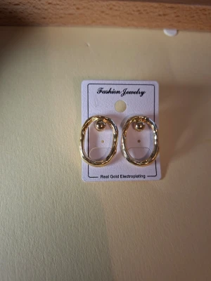 Guldpläterade ovala örhängen - Snygga ovala örhängen i guldplätering med en lätt vågig design. De har en enkel men trendig look och fästs med plupp. Perfekta för dig som gillar stilrena accessoarer med en twist.