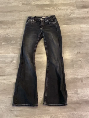 Svarta bootcut jeans  - Ett par svarta bootcut jeans från Gina Tricot med vita kontrastsömmar och dekorativa bakfickor. Jeansen har låg midja och klassisk femficksdesign. Materialet är denim med lätt tvättade detaljer för en cool look.