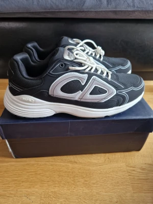 Svarta sneakers med vita detaljer - Snygga svarta  sneakers med vita detaljer och stora CD-loggor på sidan. Skorna har vita snören, meshpaneler för extra ventilation och en tjock vit sula med Perfekta för dig som vill ha en trendig och exklusiv look.