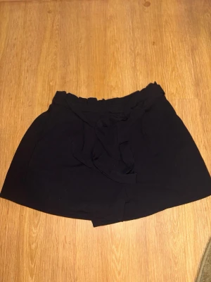 Svarta shorts med knyt från Stradivarius - Snygga svarta shorts från Stradivarius med hög midja och knytband i midjan. De har en avslappnad passform och är perfekta för varma dagar. Tillverkade i ett mjukt och lätt material som känns skönt mot huden.