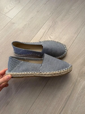 Randiga loafers från Primark - Säljer ett par snygga loafers från Primark med marinblå och vita ränder. Skorna har en klassisk espadrille-look med flätad sula i jute och ovandel i tyg. Perfekta för en avslappnad och stilren look till sommaren.