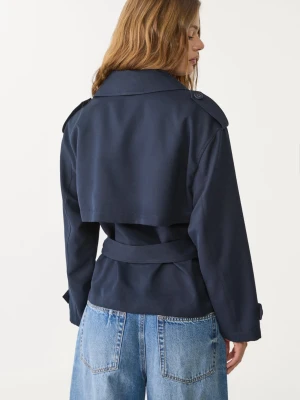 Mörkblå kort trenchcoat med bälte - Kort trenchcoat i mörkblått från Stradivarius med klassisk krage, axelklaffar och knytskärp i midjan. Jackan har dubbelknäppning och justerbara ärmslut. Perfekt för en stilren look under vår och höst. Aldrig använd