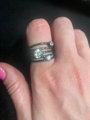 Svart ring med tre stenar - Cool ring i svart metall med flera tunna band som sitter ihop och tre glittrande stenar i olika storlekar. Ringen har en modern och edgy design som sticker ut och passar perfekt för dig som gillar unika accessoarer.
