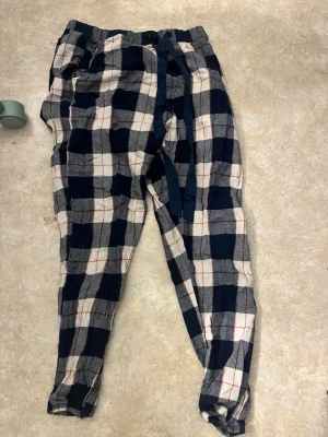 Rutiga pyjamasbyxor hunkemöller - Mysiga pyjamasbyxor i bomull med stort rutmönster i mörkblått, vitt och röda linjer. Byxorna har resår i midjan och en justerbar dragsko för extra komfort. Perfekta för slappa dagar hemma.