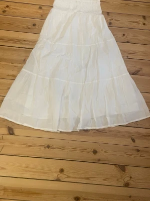 Vit långkjol från Gina Tricot - Luftig och flowy vit långkjol från Gina Tricot med smock i midjan. Kjolen har flera lager och en lätt rynkad struktur som ger en avslappnad och somrig vibe. Perfekt för varma dagar och enkel att matcha med olika toppar.