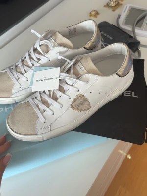 Vita Philippe Model sneakers med gulddetaljer - HELT NYA Philippe Model skor. Köpte fel storlek därför säljer jag de annars älskar jag de. Används en gång (när jag testa de) Köptes för 3500