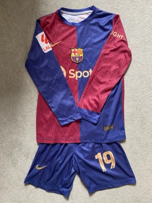Barcelona matchställ 24/25 Lamine Yamal #19 - Säljer ett FC Barcelona matchställ 2024/25 med långärmad tröja från Nike med Lamine Yamal #19 på ryggen. Tröjan har klubbmärke och sponsorloggor på bröstet samt tryck på ärmarna. Det finns en eller två utstickande trådar dock. Tillverkat i lätt och ventilerande material, perfekt för fotboll! 