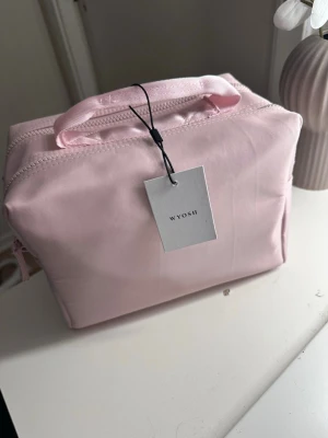 Ljusrosa necessär från Wyosh - Söt ljusrosa necessär från Wyosh med dubbla dragkedjor och praktiskt handtag upptill. Tillverkad i ett slätt tygmaterial som känns lätt och smidigt att bära med sig. Perfekt för att organisera smink eller småprylar i väskan.