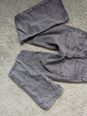 Gina Tricot grå bootcut jeans storlek 164 - Säljer ett par grå jeans med bootcut passform och klassisk femficksdesign från Gina Tricot. Jeansen har låg midja, bälteshällor och dragkedja med dubbla knappar. Perfekta för en avslappnad och trendig look. Från barnavdelningen på Gina Tricot i storlek 164, i vuxen storlek blir det xs/s. Mycket fint skick och inga synliga defekter.