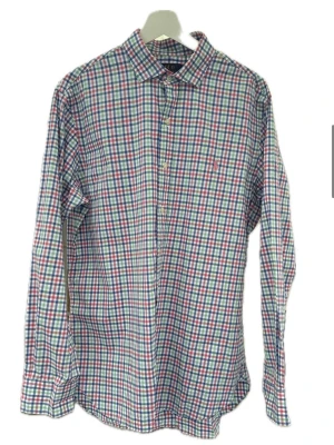 Rutig skjorta från Polo Ralph Lauren - Klassisk rutig skjorta från Polo Ralph Lauren i bomull. Skjortan har lång ärm, knappar framtill och en liten broderad logga på bröstet. Färgkombinationen är vit, blå, grön och röd vilket ger en fräsch och tidlös look.