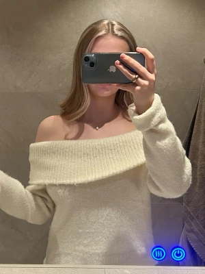 Off shoulder stickad tröja cremevit - Superfin off shoulder stickad tröja i cremevitt med bred ribbad kant upptill. Tröjan har lång ärm och är gjord i ett mjukt, fluffigt material som känns riktigt cozy.