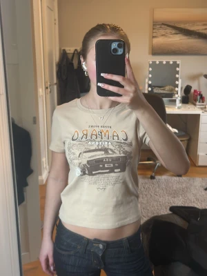 Beige Camaro t-shirt med biltryck - Cool beige t-shirt med Camaro-tryck och motiv av en klassisk bil framtill. T-shirten är kortärmad och har en croppad passform som ger en trendig look. Använd max 5 gånger så väldigt bra skick! Storlek xxs och säljer då den tyvärr inte kommer till användning. 💕