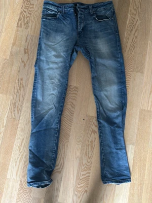 Neuw Slim Jeans - Snygga blå slim fit jeans med tvättade partier på låren och knäna. Klassisk modell med knappar i midjan. Jeansen har en modern passform och är perfekta för en avslappnad stil. Byxorna är W33 och L32. Hör av er vid några frågor!