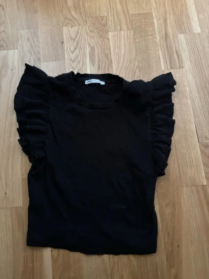 Svart volangärmad topp från Zara - Snygg svart topp från Zara med volangdetaljer på ärmarna och ribbad struktur. Modellen är croppad och har en rund halsringning. Perfekt för dig som vill ha en trendig och stilren look. Inte använd på flera år, och inga defekter💕💕