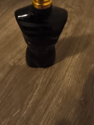 Jean Paul Gaultier Le Male parfym - En ikonisk parfymflaska från Jean Paul Gaultier formad som en svart manlig torso med guldfärgad kork. Flaskan har en matt finish och är tillverkad i glas. Perfekt för dig som gillar unika och snygga parfymflaskor.
