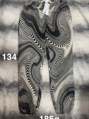 Svartvita byxor med psykedeliskt mönster - Unika byxor i svart och vitt med ett riktigt psykedeliskt, vågigt mönster. Byxorna har resår i midjan och vid bensluten för en skön passform. Perfekta för dig som vill sticka ut och gillar grafiska prints. 🌸 Ny med lapp. Storlek 134