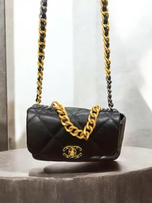  svart axelväska i läder - Snygg svart axelväska i läder, Väskan har en mixad kedjerem i svart och guld samt en chunky guldkedja som detalj. Perfekt för dig som gillar lyxig och tidlös design.