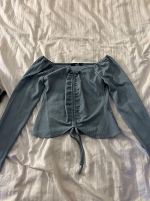 Ljusblå offshoulder topp från Bik Bok - Trendig ljusblå offshoulder topp från Bik Bok med långa ärmar och ribbad struktur. Toppen har snygg snörning framtill