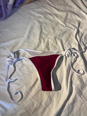 NY Vinröd bikiniunderdel med knyt - NY! Snygg vinröd bikiniunderdel med vita kanter och knyt i sidorna. Perfekt för stranden eller poolen och ger en trendig look. Klassisk trekantsform som framhäver figuren.