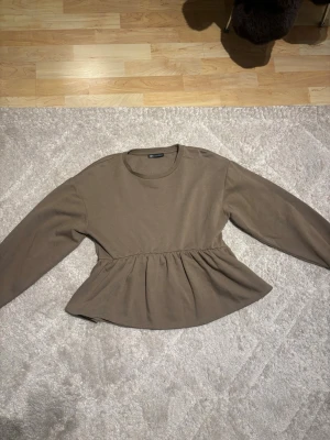 Grön peplum topp från Zara storlek S/M - Säljer en grön peplum topp från Gina Tricot med rund halsringning och långa ärmar. Toppen har en markerad midja med rynkade detaljer som ger en snygg siluett. Perfekt att styla med jeans eller kjol för en trendig look.