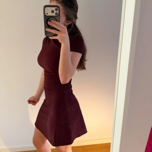 Vinröd kort klänning med glitter - Säljer en glittrig vinröd kort klänning med tight passform upptill. 