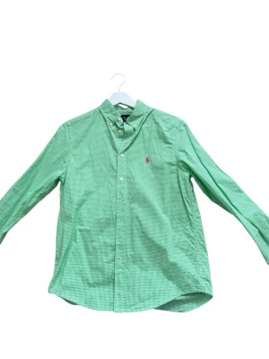 Grön rutig skjorta från Ralph Lauren - Snygg grön skjorta från Ralph Lauren med små rutor och klassisk button-down krage. Skjortan har lång ärm, knappar framtill och den ikoniska rosa loggan broderad på bröstet. Tillverkad i mjuk bomull som känns skön mot huden. Passar mellan 162/172cm lång hör av er vid frågor eller funderingar. Pris kan diskuteras 