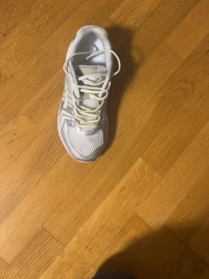 Vita mesh sneakers med silvriga detaljer - Snygga vita sneakers med silvriga detaljer och meshpaneler för extra ventilation. Skorna har klassisk snörning och låg profil. Perfekta för dig som gillar sportig stil och vill ha bekväma skor till vardags. Yttermaterialet är en mix av syntet och mesh.