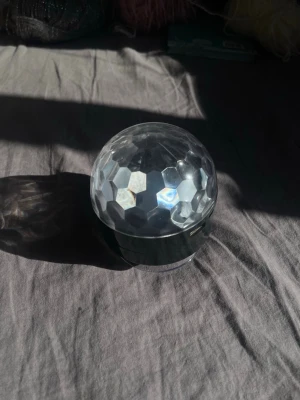 Discolampa med prismakupol - Säljer en liten discolampa med genomskinlig prismakupol och silverfärgad bas. Lampan har en rund form och skapar coola ljuseffekter när den är igång. Perfekt för att höja stämningen på hemmafester eller i ungdomsrummet.