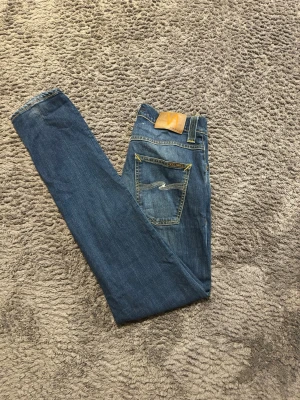 Nudie Jeans Grim Tim - Snygga blå slim fit-jeans från Nudie Jeans i modellen Grim Tim i storlek 29/32. Jeansen har en skön passform och slitningar på låren som ger en avslappnad, lite rå känsla. Enkla att matcha och passar perfekt till vardags – oavsett om du kör t-shirt eller skjorta. 