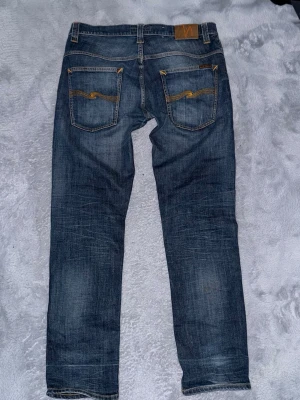 Nudie Jeans - Säljer ett par riktigt snygga Nudie Jeans i storlek W34 L32. Klassisk blå denim med snygg slitning/tvätt som ger en clean och stilren look.  ✅ Storlek: W34 L32✅ Skön passform✅ Snygg blå tvätt✅ Bra skick✅ Perfekta till vardag och fest  Jeansen är använda men fortfarande i fint skick utan större defekter. Passar till det mesta och sitter riktigt bra.  📦 Skickas snabbt💬 Hör av dig vid frågor eller om du vill ha fler bilder!