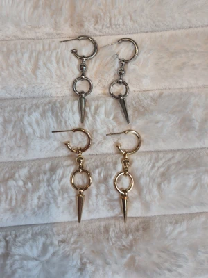Chunky örhängen med ring och spets - Säljer två par statement-örhängen i metall, ett par i silverfärg och ett par i guldfärg. Båda har en rund ring och en hängande spetsig detalj som ger en edgy look. Perfekta för att lyfta vilken outfit som helst.